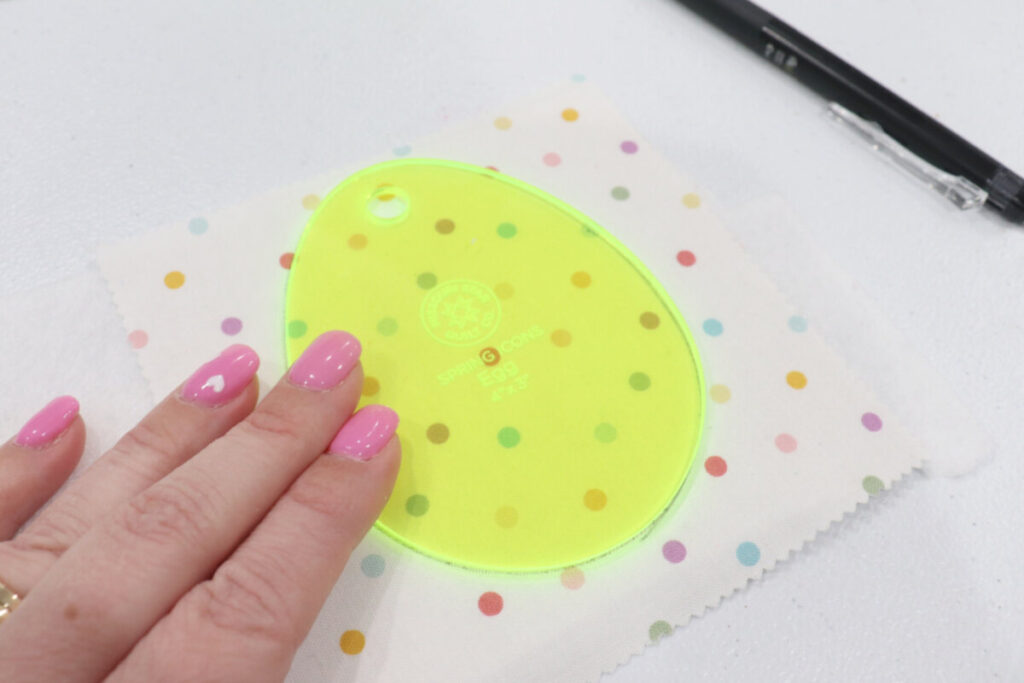 Image contains Amy’s hand holding a neon yellow egg-shaped template on top of a piece of white polka dot fabric. A black pen sits nearby.