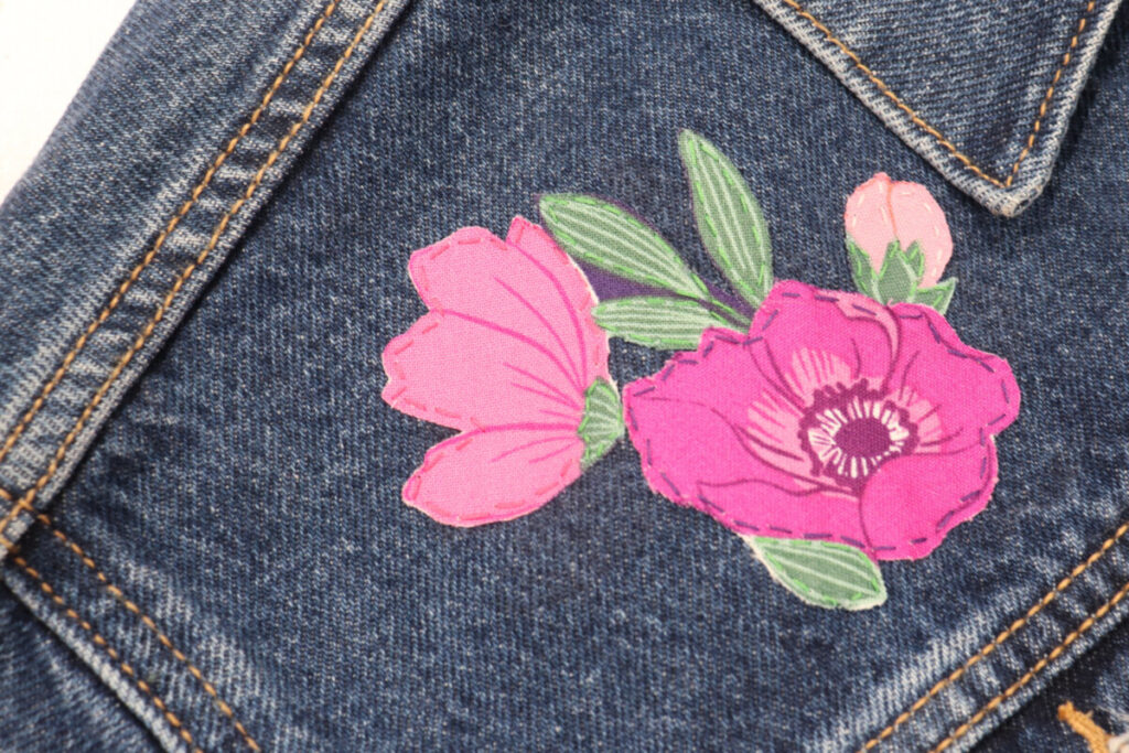 Image contains a close-up view of three pink flowers that have been ironed onto the jacket and stitched around with coordinating thread.