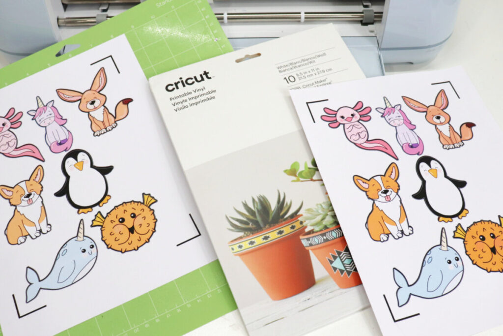 Image contains a Cricut Maker 3, a pack of Printable vinyl, a cutting mat, and two printed animal sticker sheets on a white background.