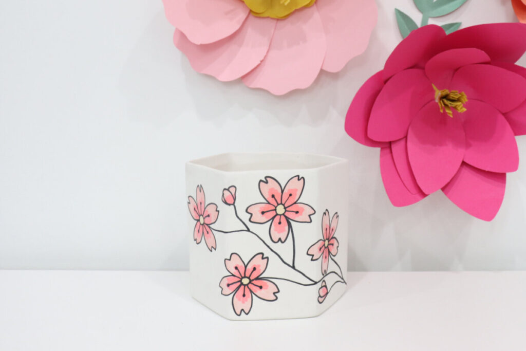 Image contains a hexagon shaped white planter decorated with hand drawn pink cherry blossoms.