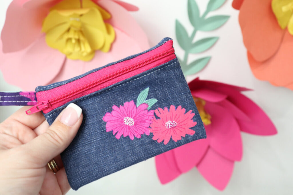 Image contains Amy’s hand holding a small denim zipper pouch with two flowers appliqued to the front.