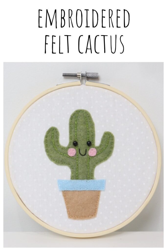 Image contains a wooden embroidery hoop with a piece of white fabric inside and an embroidered felt cactus with a smiling face.