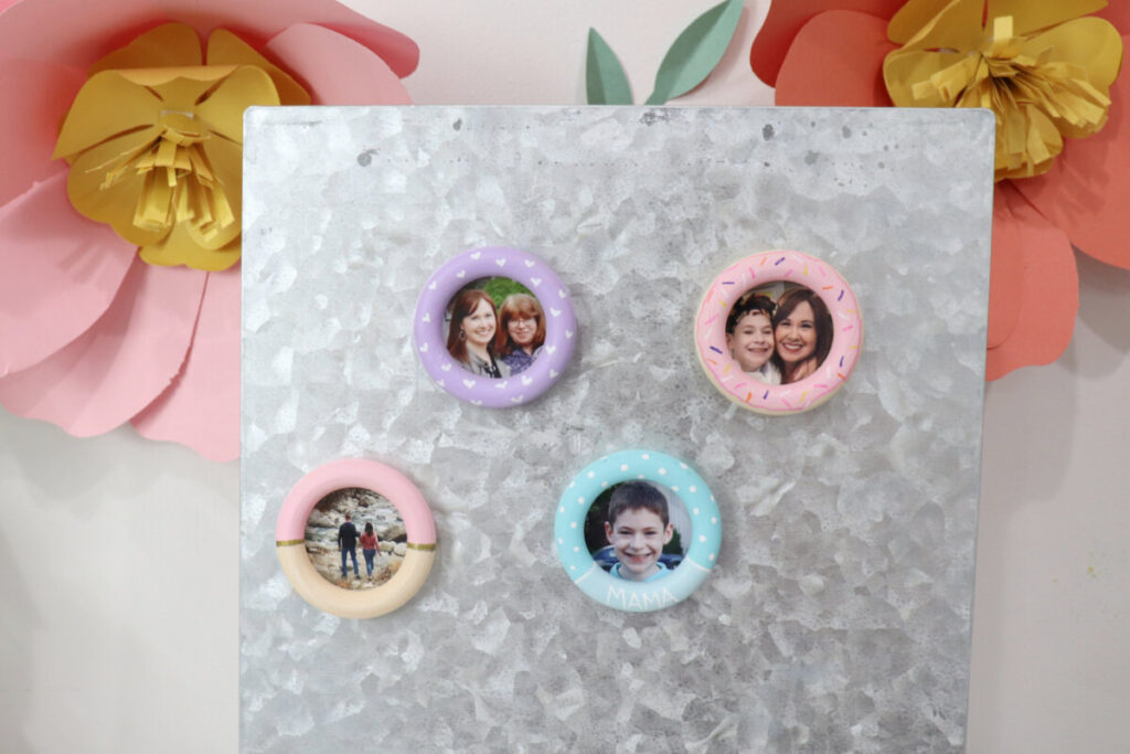 Image contains four wooden photo magnets on a silver metal surface. Large pink and orange paper flowers are on the wall behind it.