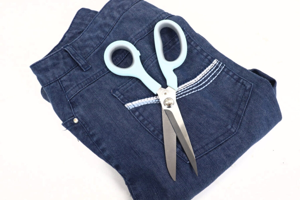 Image contains a pair of dark denim jeans with a pair of scissors sitting on top.