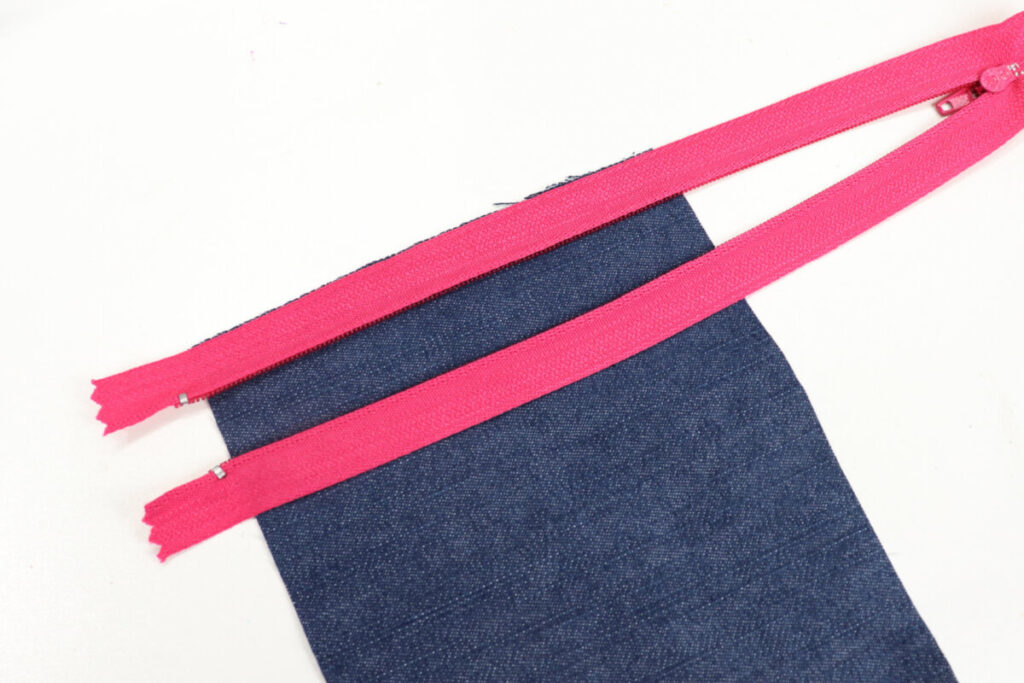 Image contains a rectangle of denim with the edge of a hot pink zipper lying upside down along the top.