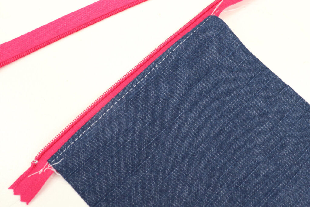 Image contains a denim rectangle sewn to one side of a hot pink zipper. 
