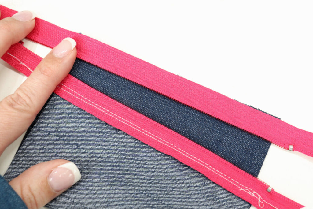 Image contains Amy’s hand holding the other edge of the hot pink zipper along the bottom edge of the denim rectangle.