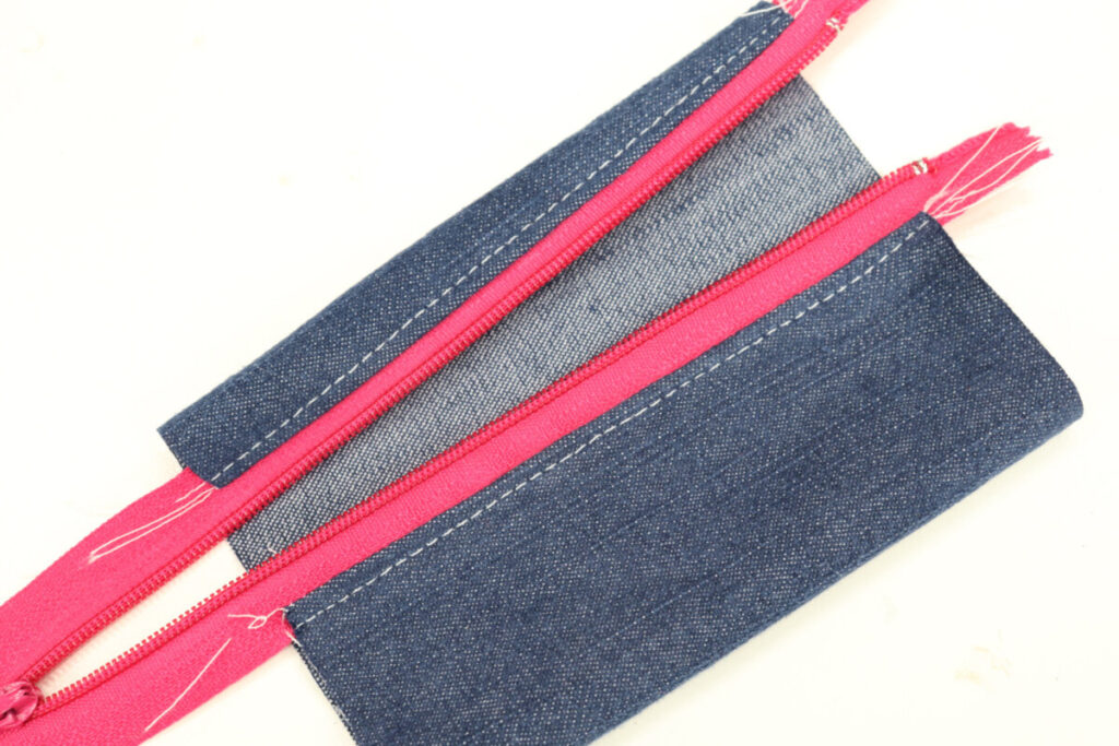 Image contains a denim rectangle with the edges sewn to a hot pink zipper.
