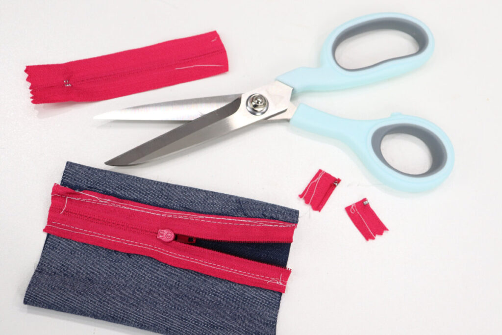 Image contains the denim and zipper tube lying inside out on a white table. A pair of scissors and the trimmed ends of the zipper sit nearby.