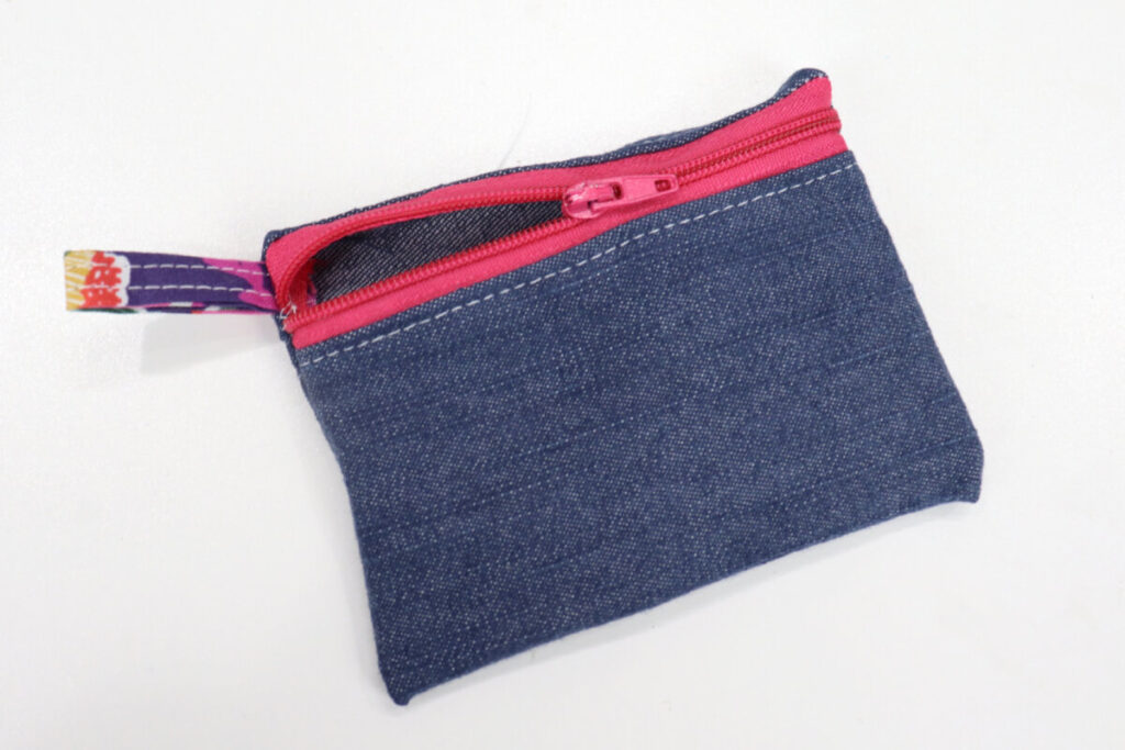 Image contains a small denim zipper pouch turned right side out sitting on a white table.
