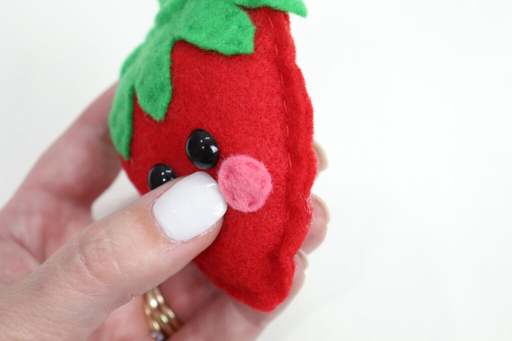 Image contains Amy’s hand holding a plush strawberry with eyes and pink cheeks.