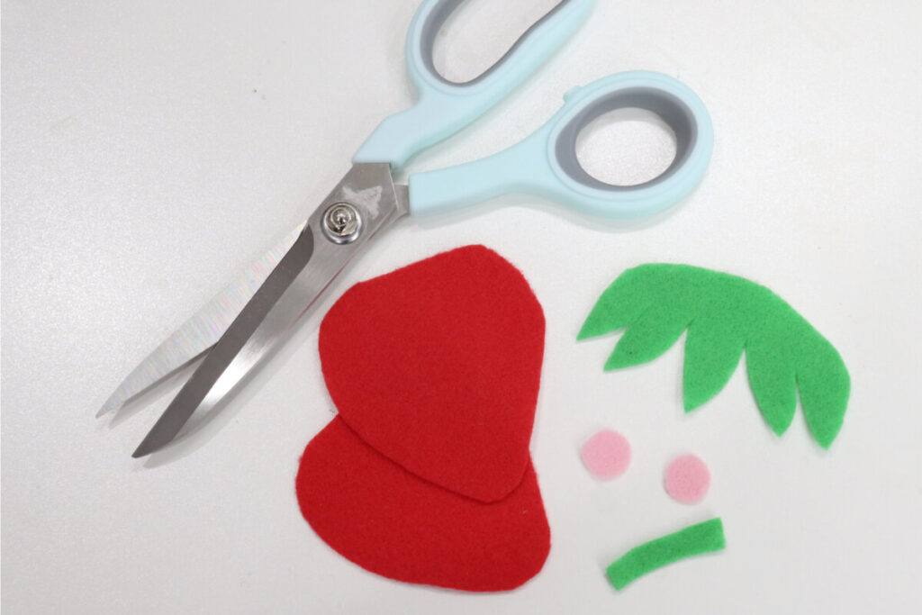 Image contains red green and pink felt shapes and a pair of light-blue handled scissors on a white background.