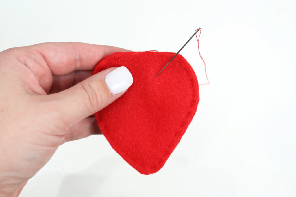 Image contains Amy’s hand holding two berry shaped pieces of red felt that have been sewn together around the sides and bottom.