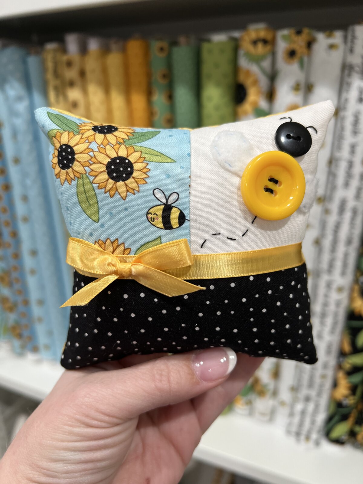 Image contains a miniature pillow with a button bee and a yellow bow, made from the Sunny Honey fabric collection.