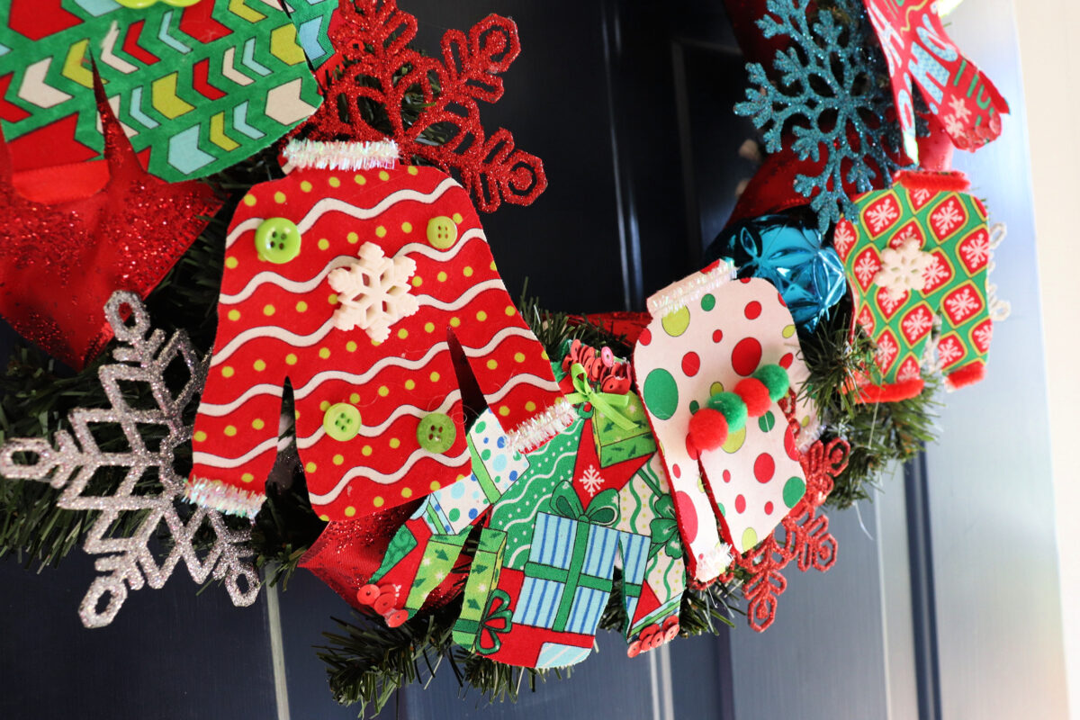 Image is a closeup view of the bottom portion of the Ugly Sweater Wreath, showing four of the fabric sweaters in detail.