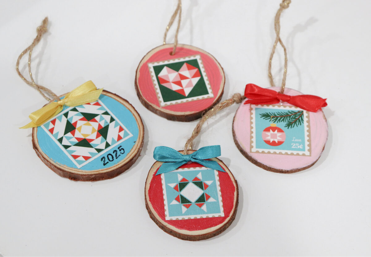Image contains four multi-colored upcycled wood slice ornaments laying on a white tabletop.