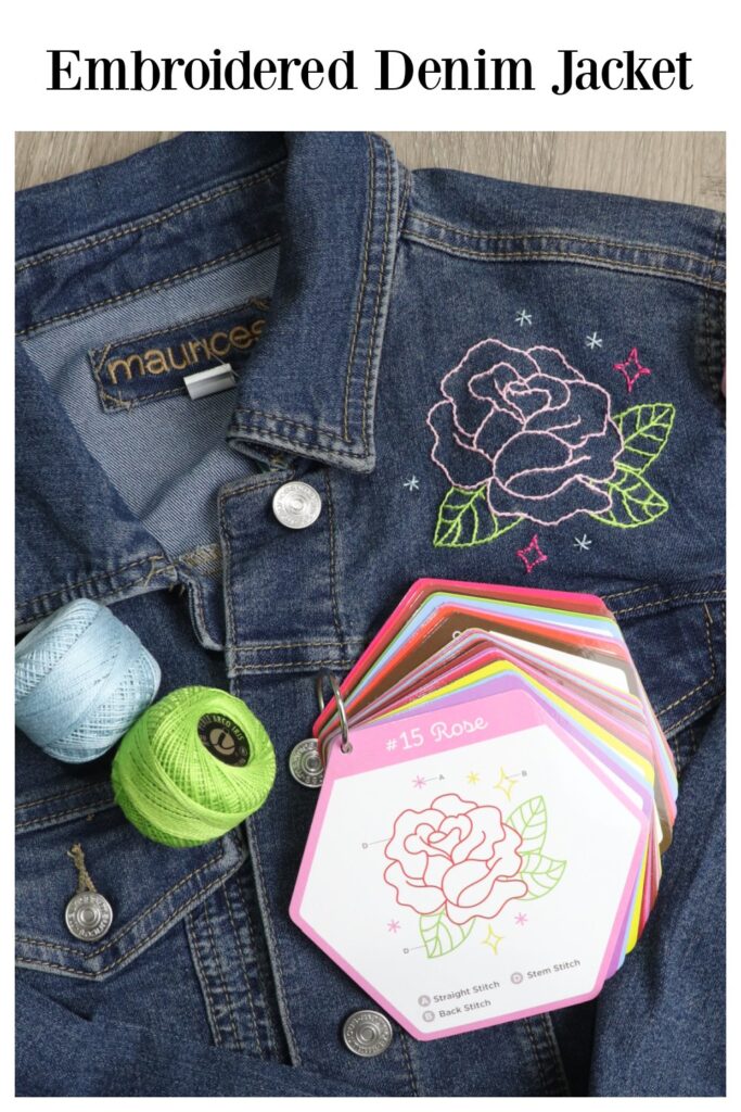 Image contains a denim jacket with a pink rose embroidered on the front. Two spools of perle cotton (blue and green) and a ring containing stitch instruction cards sit on top.