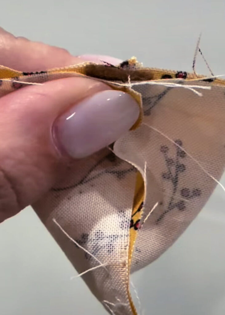 Image contains Amy’s hand holding the fabric to form a pyramid, with the tail inside the center.