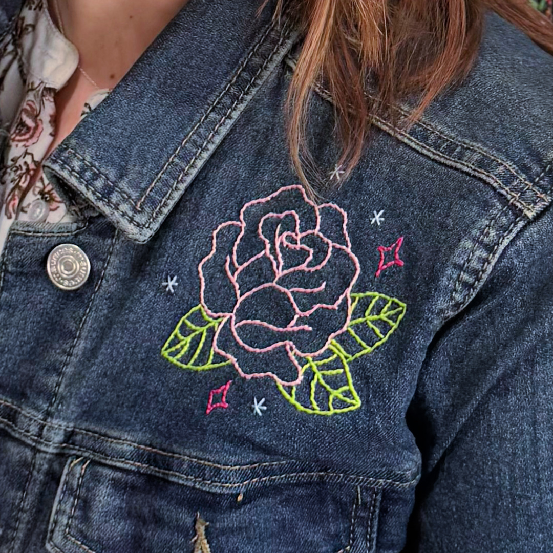 Image contains a cropped view of Amy’s shoulder. She is wearing the denim jacket, which is embellished with a pink embroidered rose.