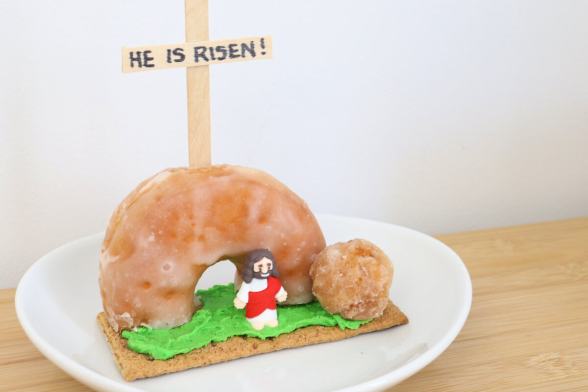 Image contains a resurrection scene made from a donut, donut hole, and graham cracker on a white plate.