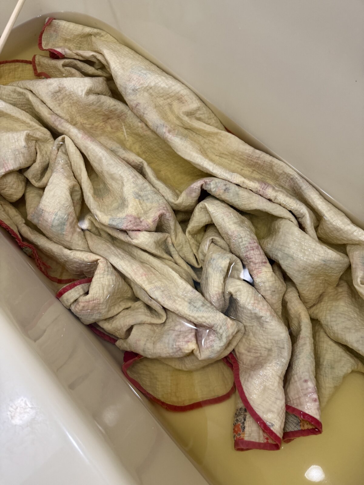 Image contains a vintage quilt in a bathtub full of dirty water.