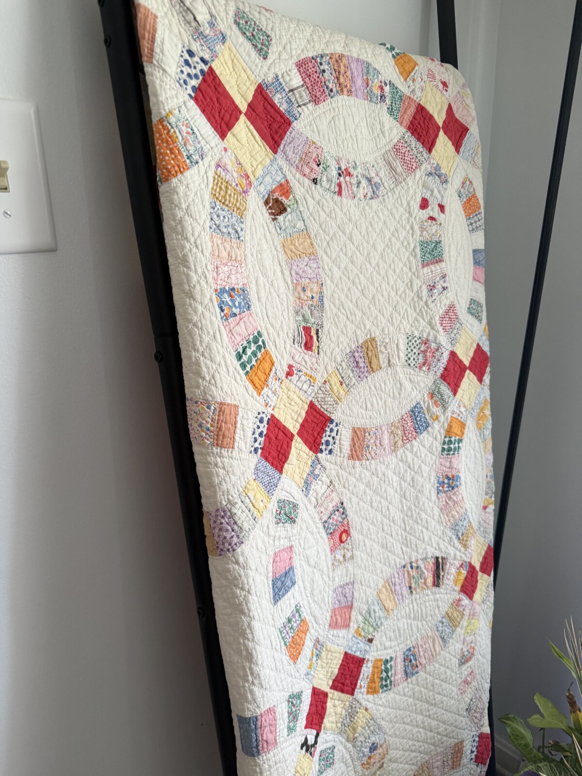 Image shows a vintage double wedding ring quilt displayed on a black metal ladder.