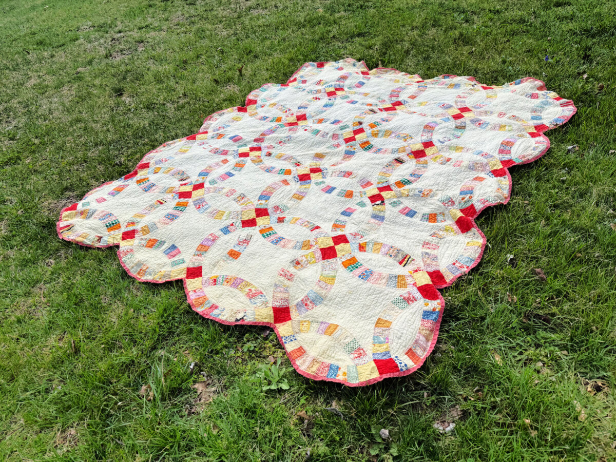 Image contains a vintage double wedding ring quilt spread out on green grass.