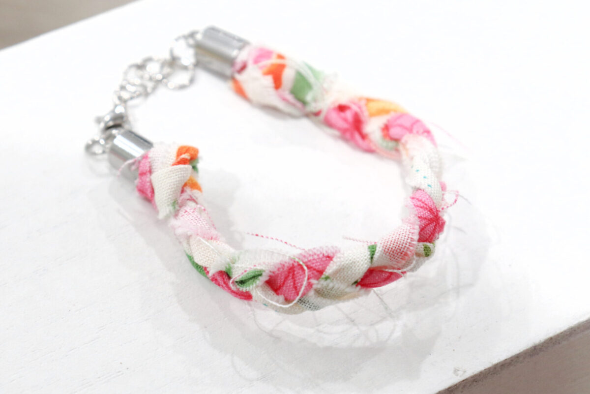This picture shows a completed bracelet made from braided fabric strips, sitting on a white surface.