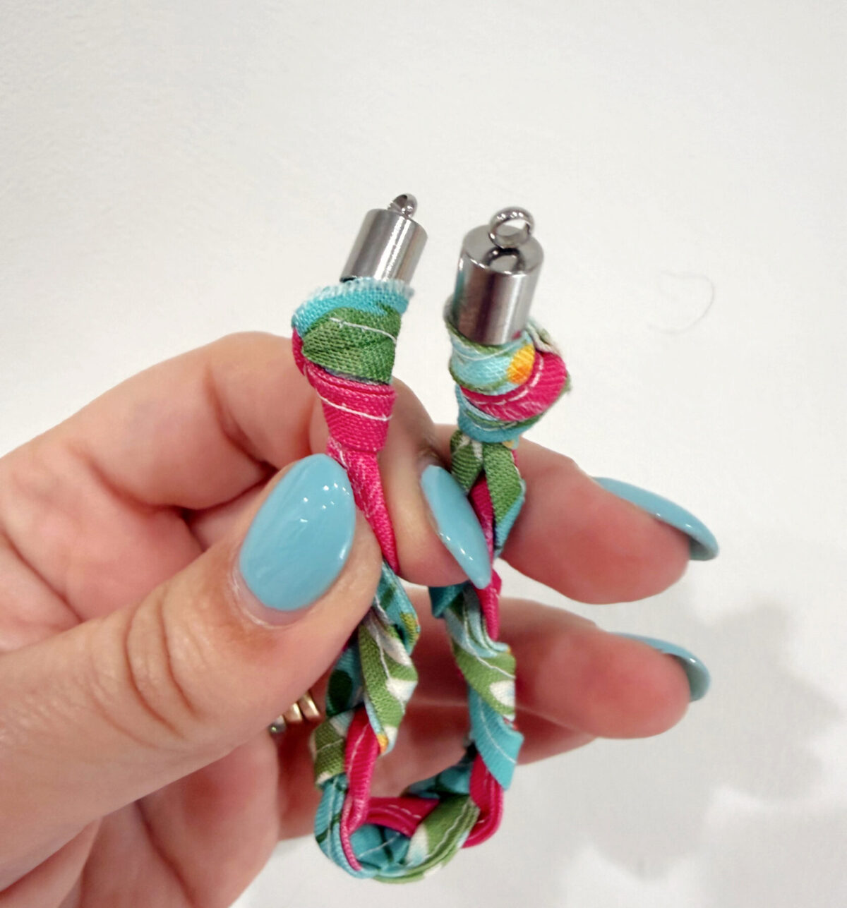 Image contains Amy’s hand holding together both ends of the bracelet with end caps attached.