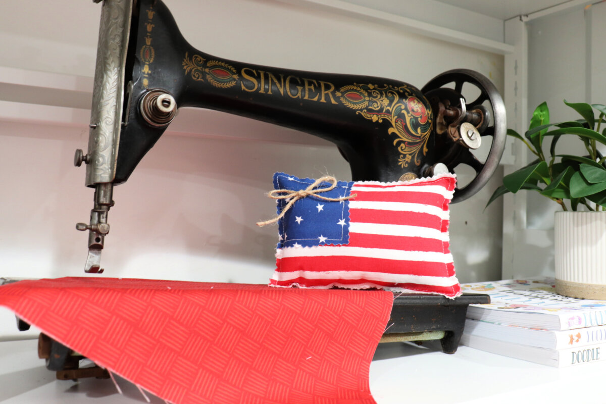Image contains a mini flag pillow sitting on a vintage Singer sewing machine.
