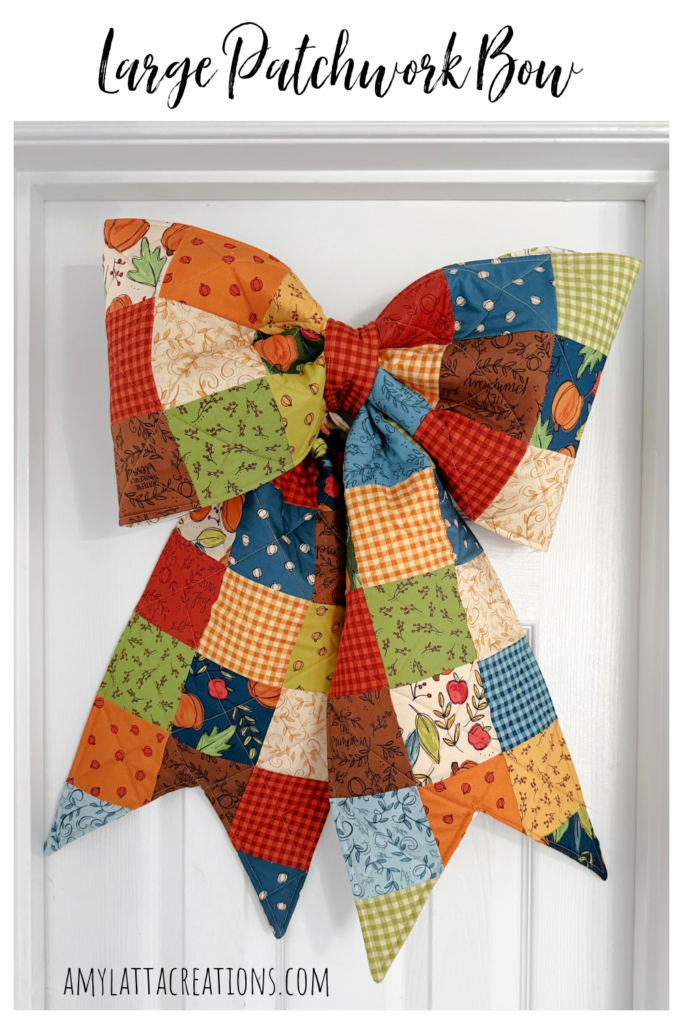 Image contains a large fabric patchwork bow made from fall fabrics, hanging on a white door.