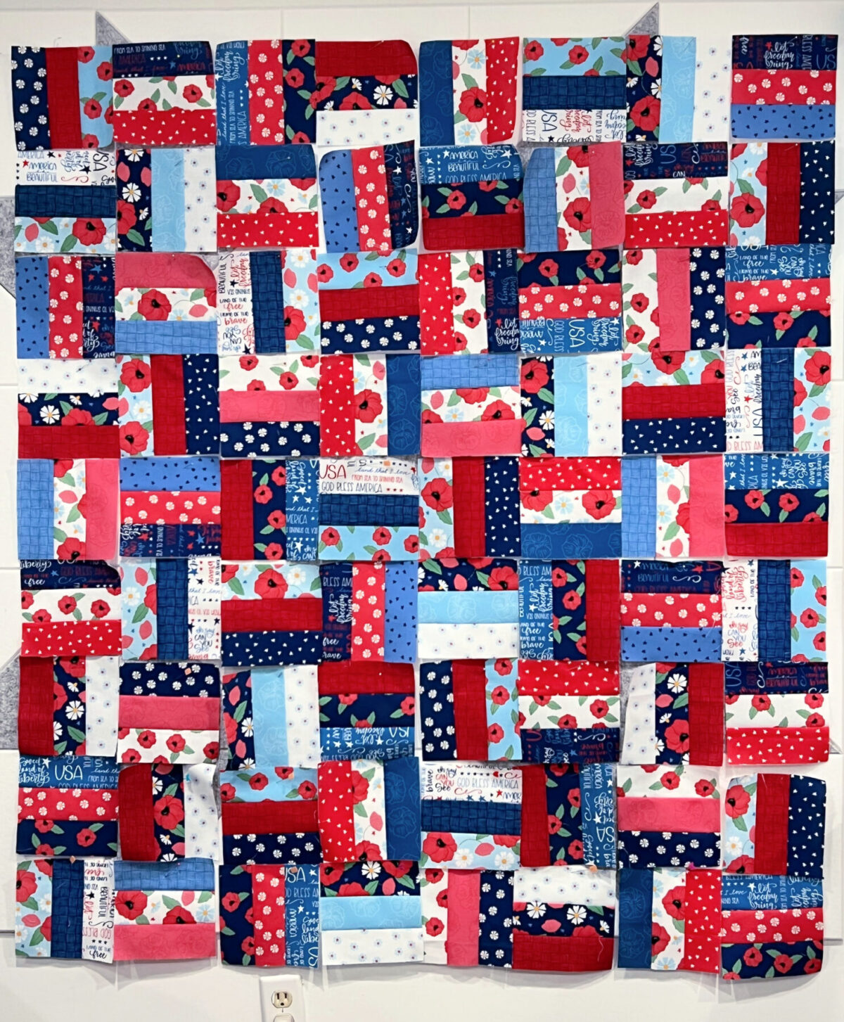 Image contains red, white, and blue quilt blocks laid out to form a quilt top on a quilt wall.