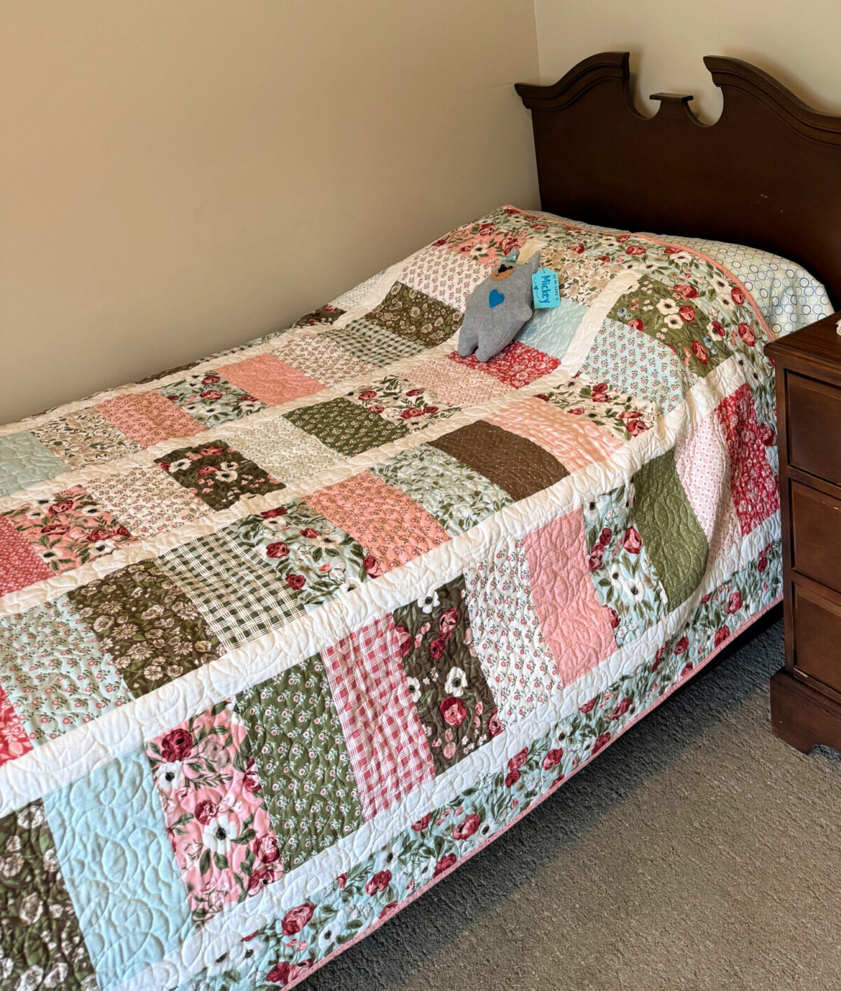 Image contains a quilt made of floral fabrics draped over a bed.