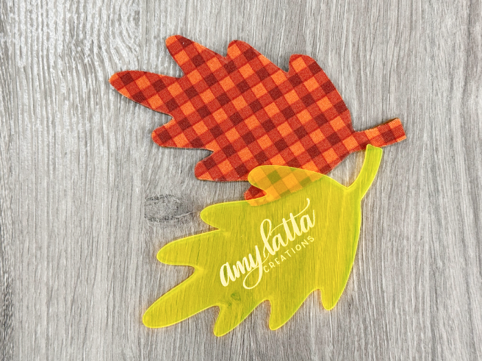 Image contains a leaf shaped acrylic template and a fabric leaf shape cut from orange gingham fabric on a wooden desk.