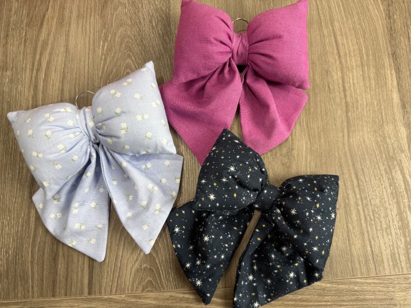 Image contains three fabric bows on a wooden table.
