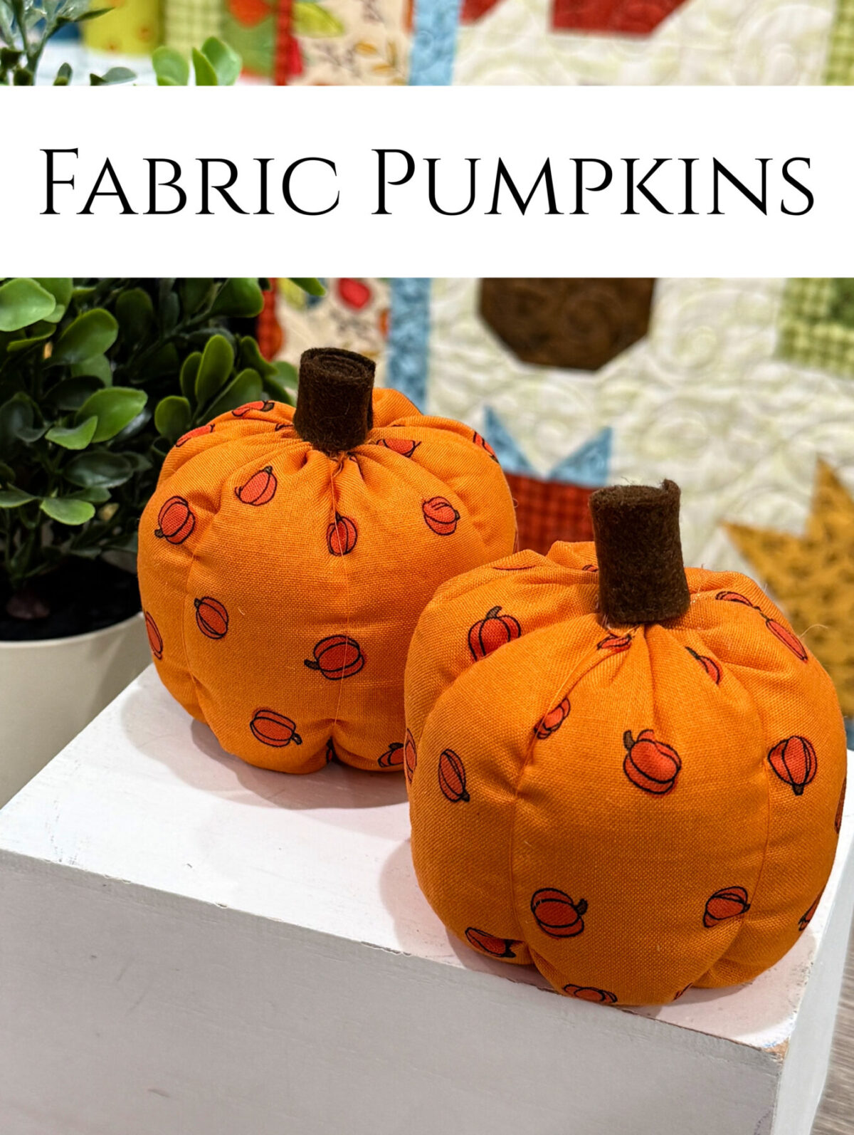 Image contains two small pumpkins made from orange fabric sitting in front of a fall themed quilt.