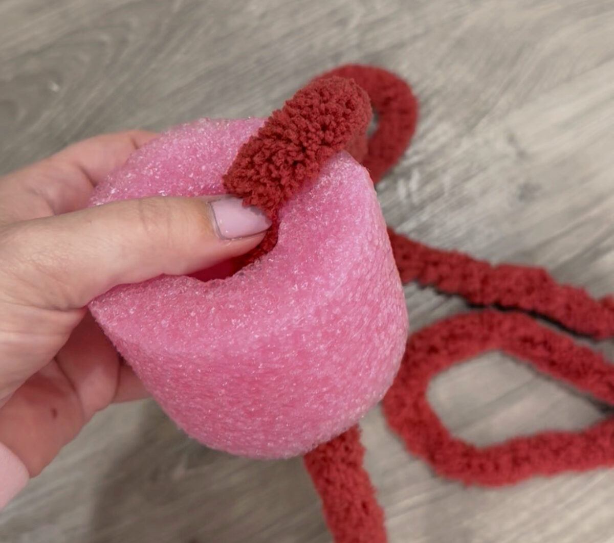 Image contains Amy's hand holding a pink 3" section of a pool noodle. Red chenille yarn is tucked inside the center.